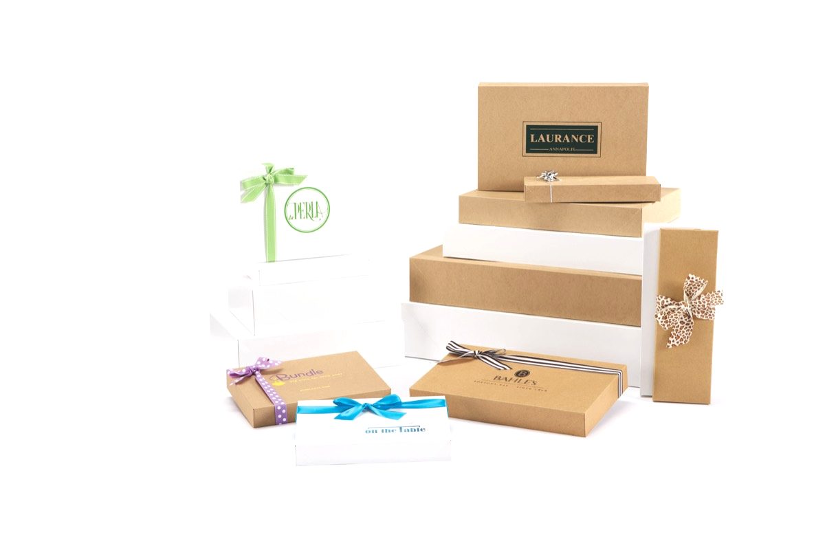 Stacked white and natural kraft apparel boxes in graduated sizes, several finished with ribbon and bows