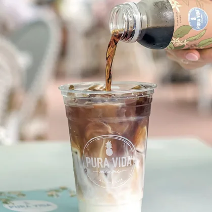 Custom printed clear plastic cup with a cafe logo being filled with iced coffee