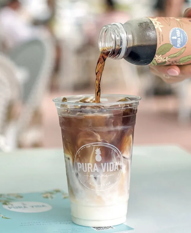 Custom printed clear PET cup for an all-day cafe being filled with iced coffee
