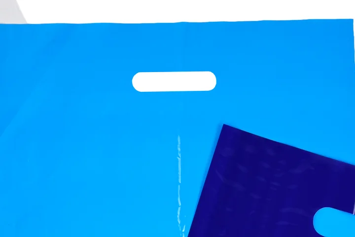 Close up of a die cut handle punched through a light blue plastic bag