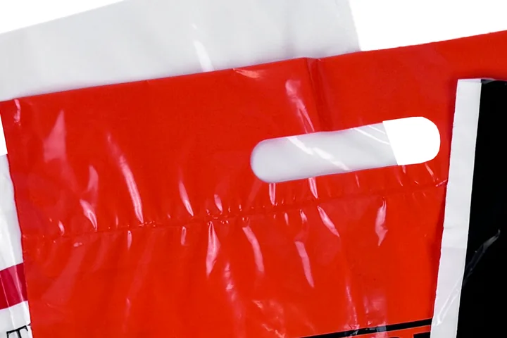 Close up of a fold over die cut handle on a red plastic bag showing the sealed fold line below the hand hole