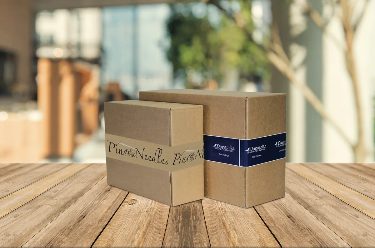Two shipping cartons sealed with custom printed packing tape, one kraft water activated tape and one navy poly tape with a logo