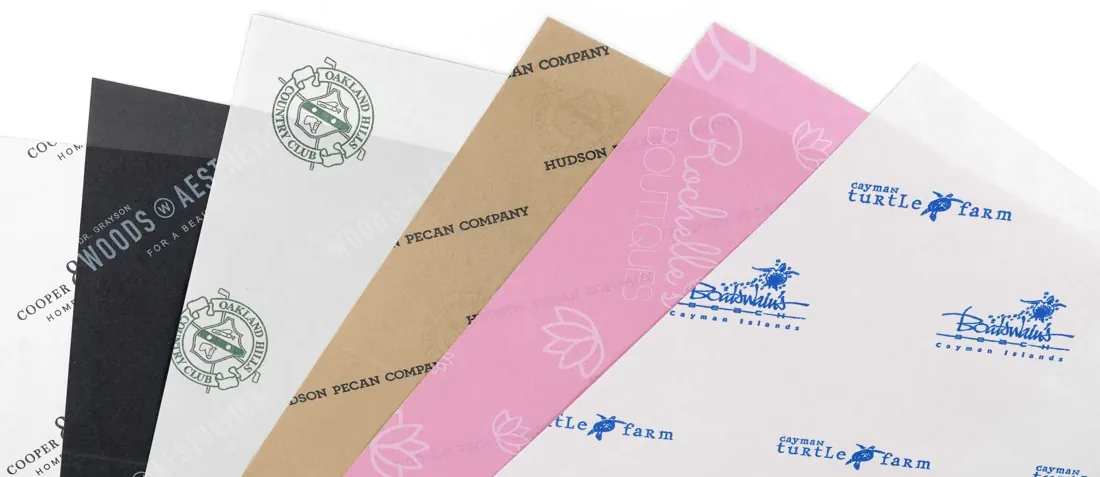 Custom printed tissue paper sheets fanned out, each printed with a different customer logo