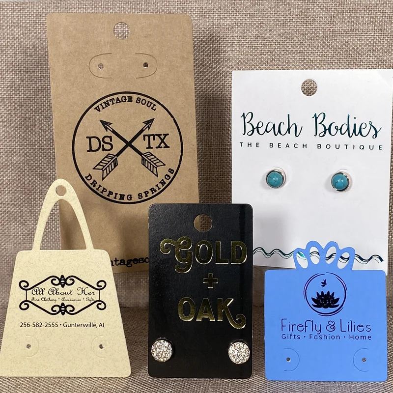 Custom printed earring cards in kraft, black, white, and blue with hot-stamped logos and stud earrings